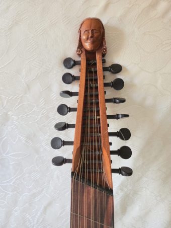Pegbox of a Robert Hadaway bandora carved as a human head, with two rows of wooden friction pegs holding the courses
