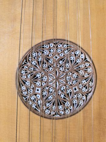 Detail of the intricate multi-layered carved rosette of a Robert Hadaway bandora with floral patterns and wire strings