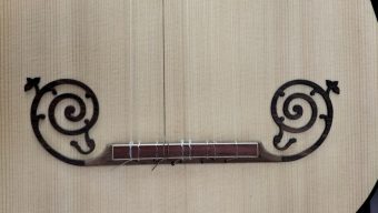 Close-up of the baroque guitar bridge with decorative moustache scroll inlays and the strings tied on