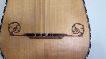 Bridge of the Régis Floury baroque guitar with the strings tied on, flanked by two carved scroll ornaments on the spruce soundboard