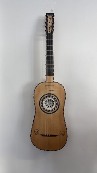 Full front view of a five-course baroque guitar by Régis Floury (2026), spruce top with parchment rosette, marquetry binding and inlaid pegbox