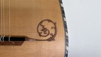 Detail of a carved scroll ornament on the soundboard of the Régis Floury baroque guitar, next to the chequered marquetry binding of the edge