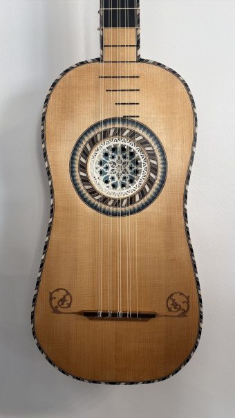 Spruce soundboard of the Régis Floury baroque guitar with parchment rosette, chequered marquetry binding and carved scroll ornaments beside the bridge